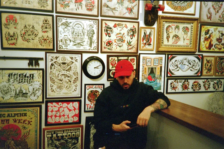 Tattoo-artiest met rode pet voor een wand vol ontwerpen